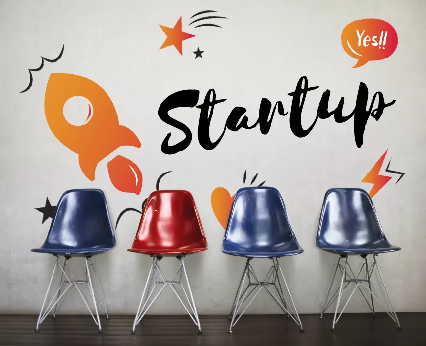 Vier Stühle in einer Reihe, einer rot und drei blau, vor einer Wand mit dem Schriftzug 'Startup' und Illustrationen einer Rakete und Sternen