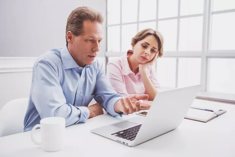 Mann und Frau sitzen vor einem Laptop und schauen betrübt.