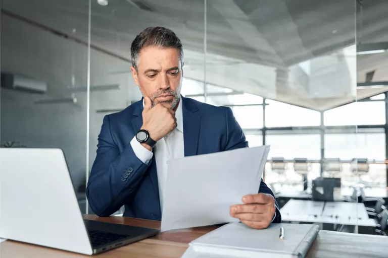 Business man betrachtet Blattpapier mit besorgtem Gesichtsausdruck