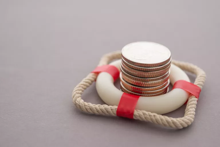Gestapelte Münzen in rotem Rettungsring oder Rettungsring mit grauem Hintergrund.