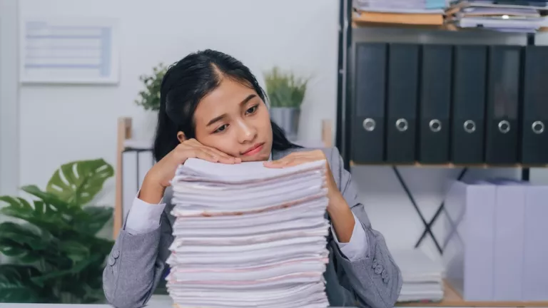 Junge Frau stützt sich über Papierstapel mit verzweifelten Blick