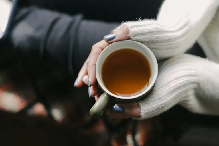 Frau mit beiden Händen um eine Teetasse